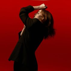 a woman with her hands behind her head, standing in front of a red background