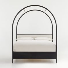 an iron bed frame with white sheets and pillows on the bottom, against a plain background