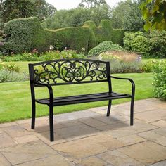 a black metal bench sitting on top of a stone walkway next to a lush green field