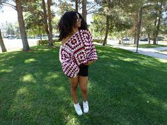 a woman standing in the grass wearing a red and white sweater