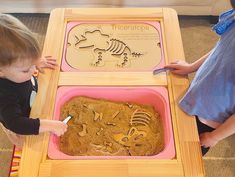 two children are playing with an animal and skeleton cookie in a play table that is made out of plywood