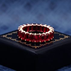 a red ring sitting on top of a black box with gold trimming around it