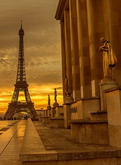 the eiffel tower in paris is lit up at sunset with statues on either side