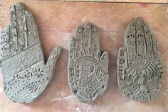 three clay hand sculptures sitting on top of a wooden table