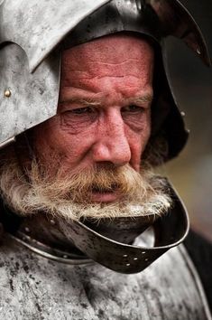 an old man with a helmet and beard wearing a suit of armor on his head