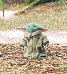 a baby yoda doll sitting on the ground in front of some grass and trees