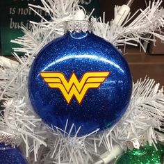 a blue ornament with the wonder woman symbol on it is hanging from a white christmas tree