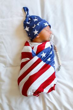 a baby wrapped in an american flag blanket sleeping on a white sheet with a telephone