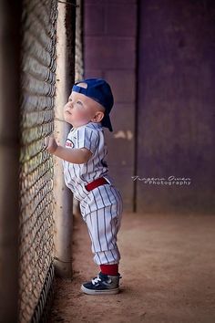 a young boy leaning against a fence wearing a baseball uniform