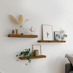 three wooden shelves with plants and pictures on them in a white living room, along with a couch