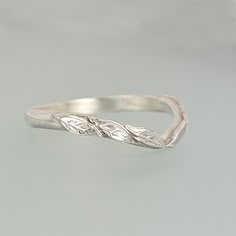 a silver ring with two leaves on the top and one leaf on the bottom, sitting on a gray surface