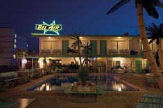 the hotel is lit up at night with palm trees in front of it and an empty swimming pool