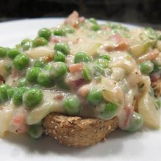 a white plate topped with green peas covered in gravy on top of bread