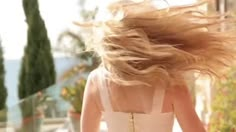 a woman walking down a street with her hair blowing in the wind and wearing a white dress