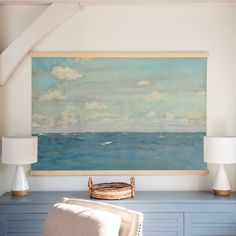 a painting hangs on the wall above a chair and lamp in a room with blue cabinets