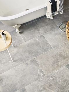 a bath tub sitting next to a wooden table on top of a tiled bathroom floor