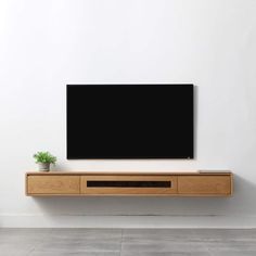 a flat screen tv mounted to the side of a white wall next to a potted plant