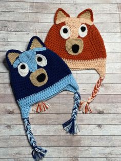 two crocheted hats with eyes and ears are on a wooden surface next to each other