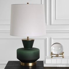 a green lamp sitting on top of a wooden table next to a white vase and mirror