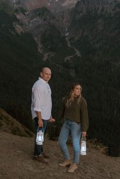 a man and woman standing on top of a mountain holding water bottles in their hands