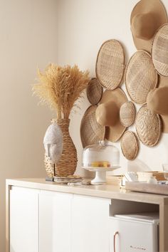 the wall is decorated with woven hats and vases on top of a white cabinet