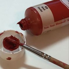 the paint is red and it has a brush in it next to an empty cup