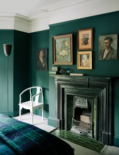 a bedroom with green walls and pictures on the wall above the fireplace, along with a white chair