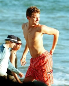 two young men walking on the beach with one man wearing red and white swim trunks