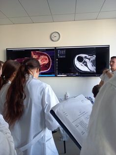 some people in white lab coats are looking at mri images on the wall behind them