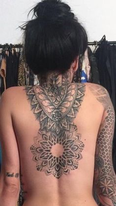 a woman with tattoos on her back standing in front of some clothes