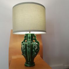 a green vase sitting on top of a wooden table next to a lampshade