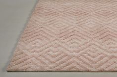 a pink rug with diamond pattern on the top and bottom side, in front of a white wall