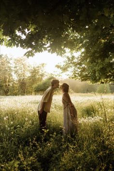 two people are kissing in the grass under a tree and some flowers on the ground