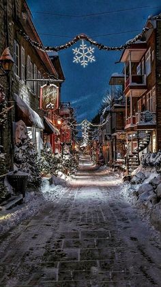 a snowy street lined with buildings and snowflakes hanging from the wires above it