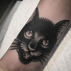 a black and white cat tattoo on the left arm, with eyes wide open showing