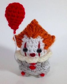 a crocheted toy with a red balloon attached to it's head, sitting on a white surface