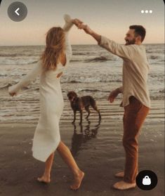 a man and woman dancing on the beach with their dog