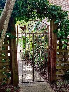 an iron gate with a butterfly on it in front of a brick wall and trees