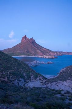 a large body of water sitting next to a mountain covered in grass and bushes on top of a lush green hillside