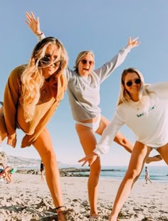 three women in bathing suits on the beach posing for a photo with their arms outstretched