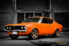 an orange muscle car parked in front of a building