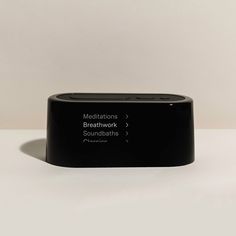 an electronic device sitting on top of a white table next to a black object with the words meditations, breakwork, and sound baths