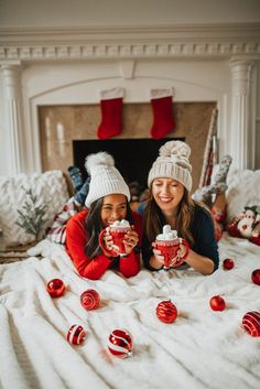 two women laying on a bed with christmas decorations and cups in front of their faces