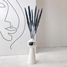 a white vase with black flowers in it next to a drawing on the wall behind it