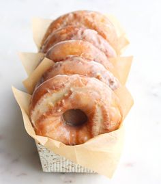 several glazed donuts sitting in a basket on top of a white tablecloth covered counter