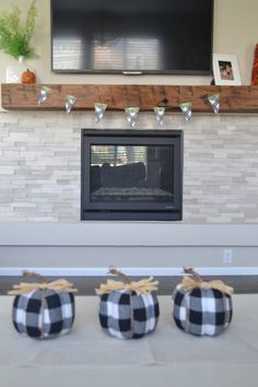 three black and white pumpkins sitting in front of a fireplace with a flat screen tv above it