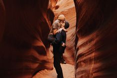 a man holding a woman in the middle of a narrow slot between two rocks and sand