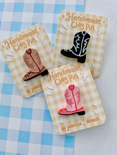 three small magnets with cowboy boots on them sitting on a blue and white checkered table cloth