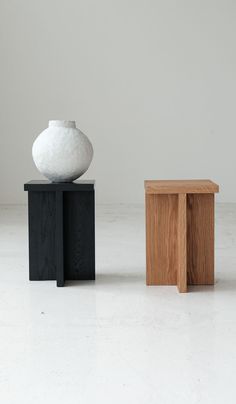 two small wooden stools sitting next to each other in front of a white vase