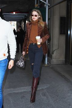 a man and woman are walking down the street with coffee in their hands while wearing boots